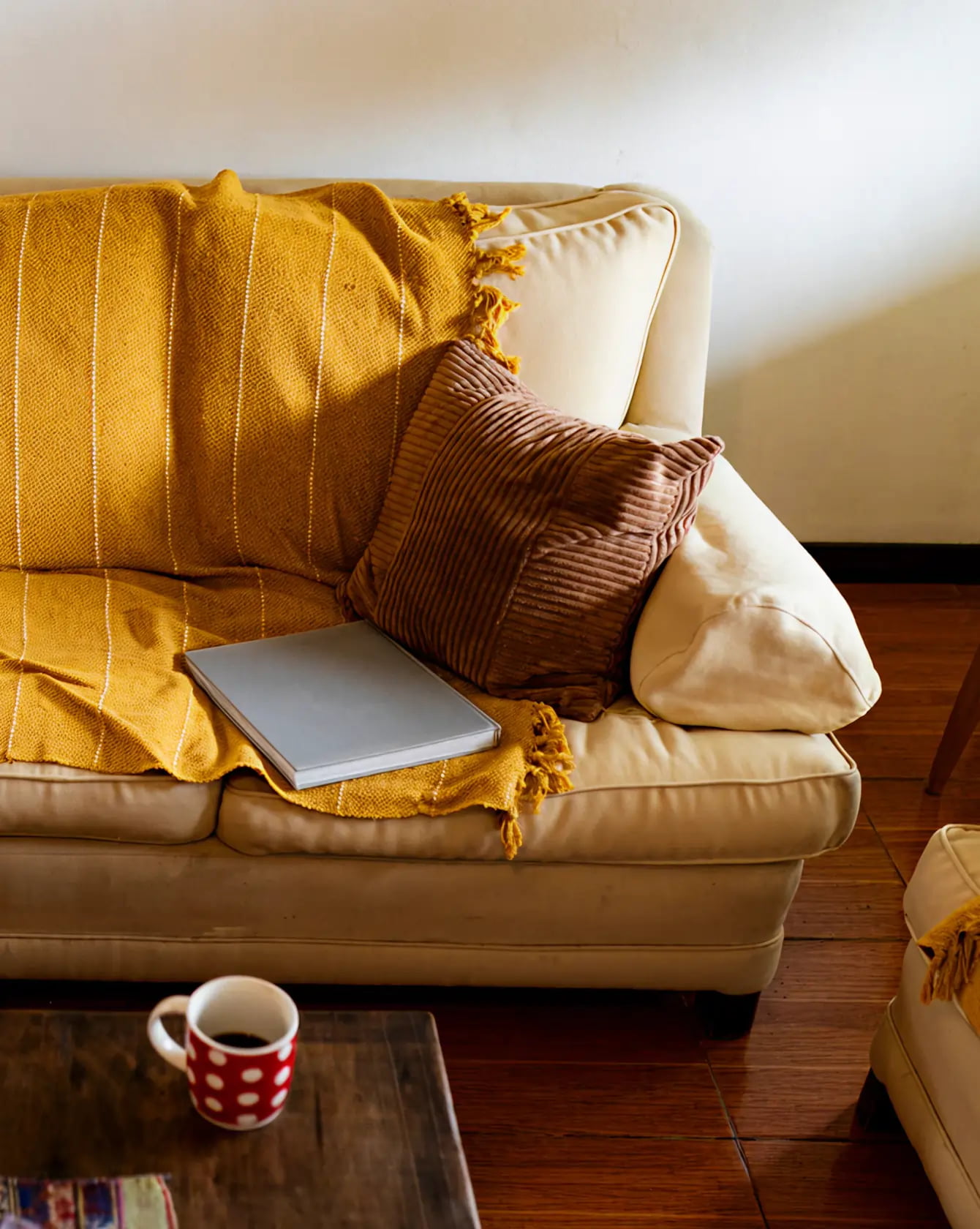 Mysig beige soffa med gul filt och kudde, en laptop och kaffekopp på bordet.